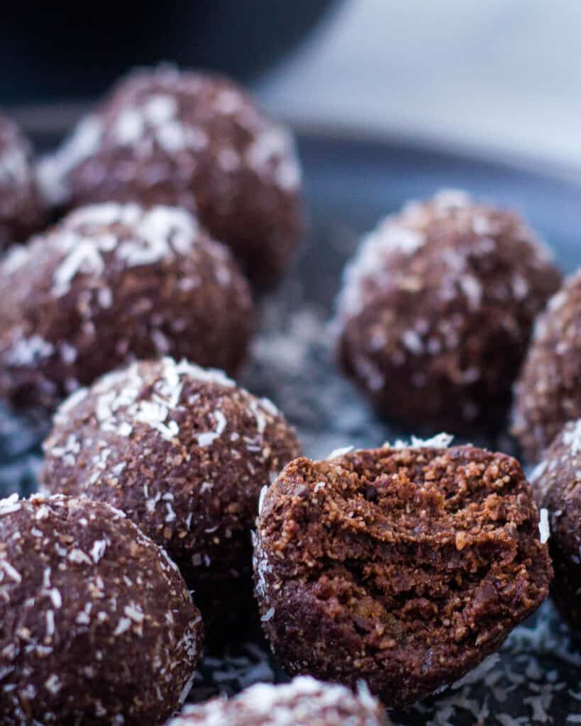Chocolate coconut date balls on black plate.