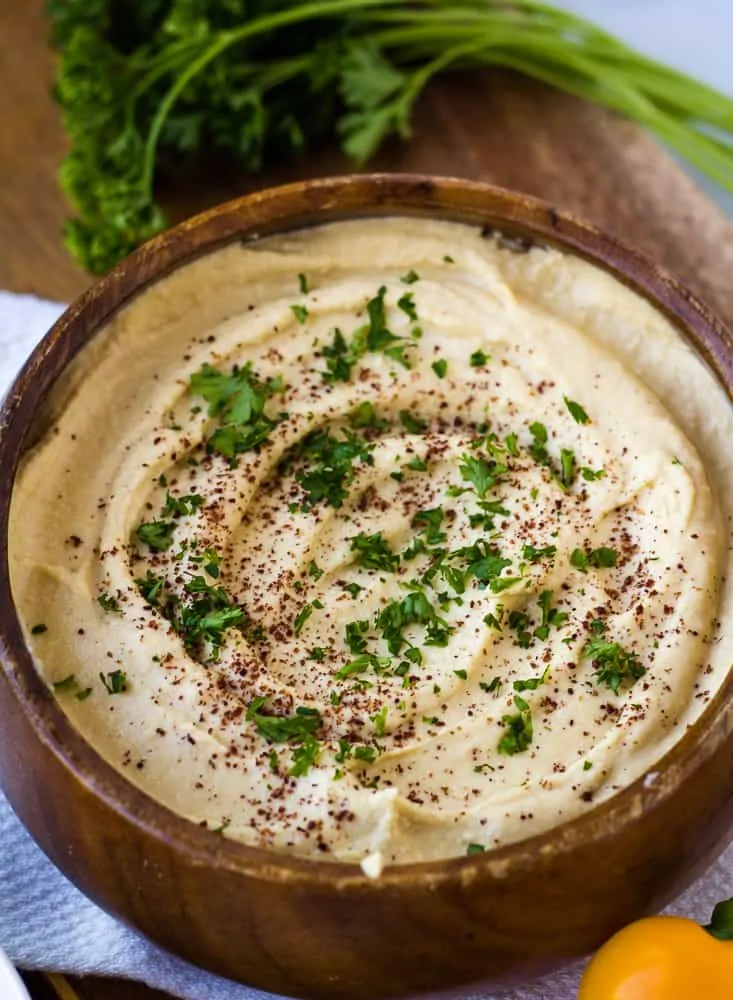 Hummus in wood bowl topped with sumac and parsley.