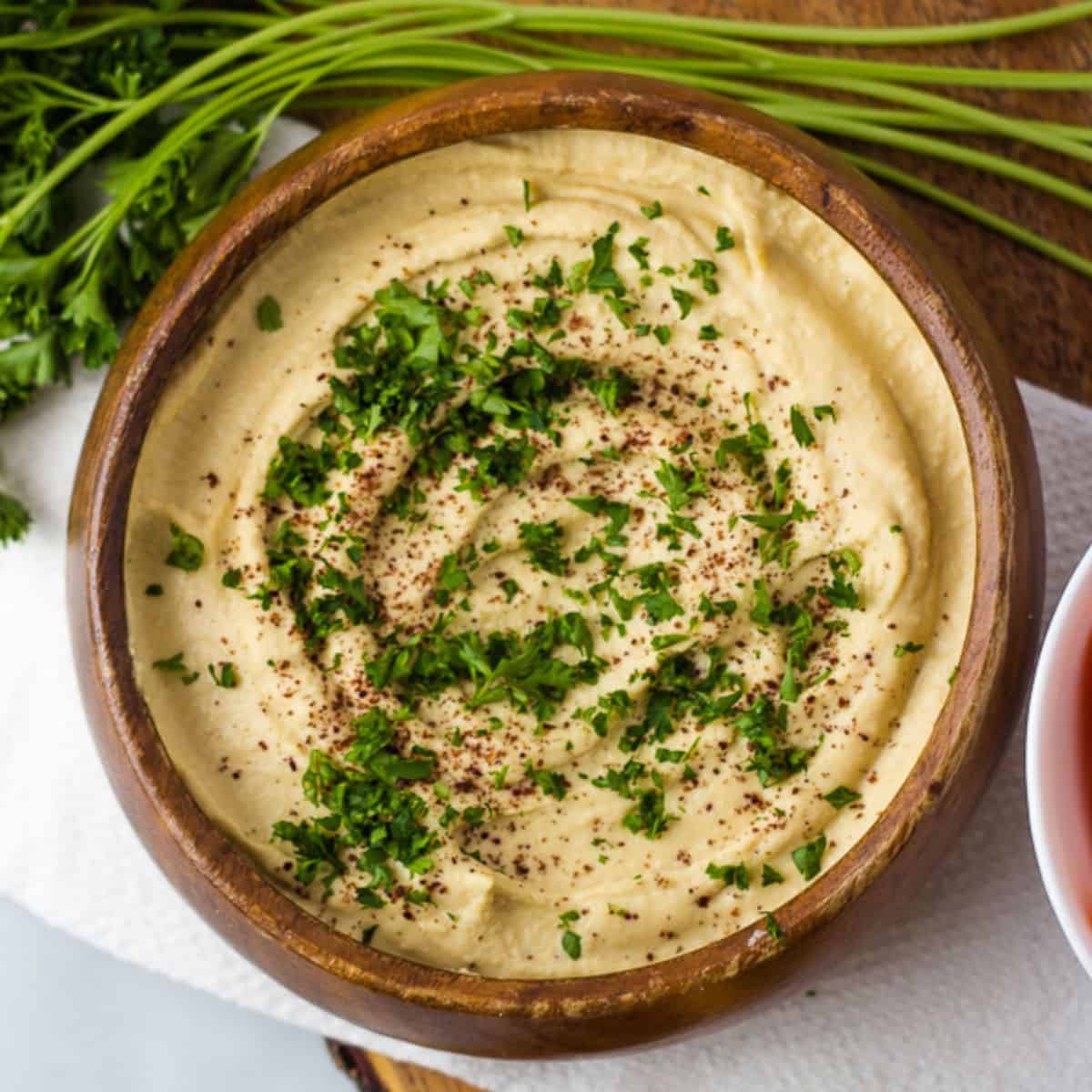 Gluten-free hummus in wood bowl topped with chopped parsley and sumac.