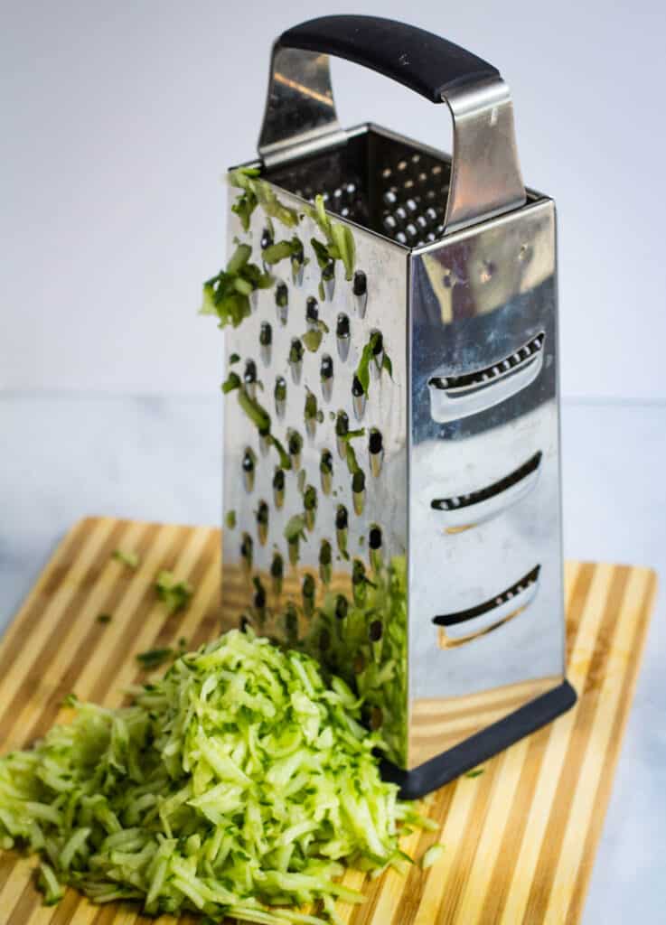 grater and grated cucumber on cutting board