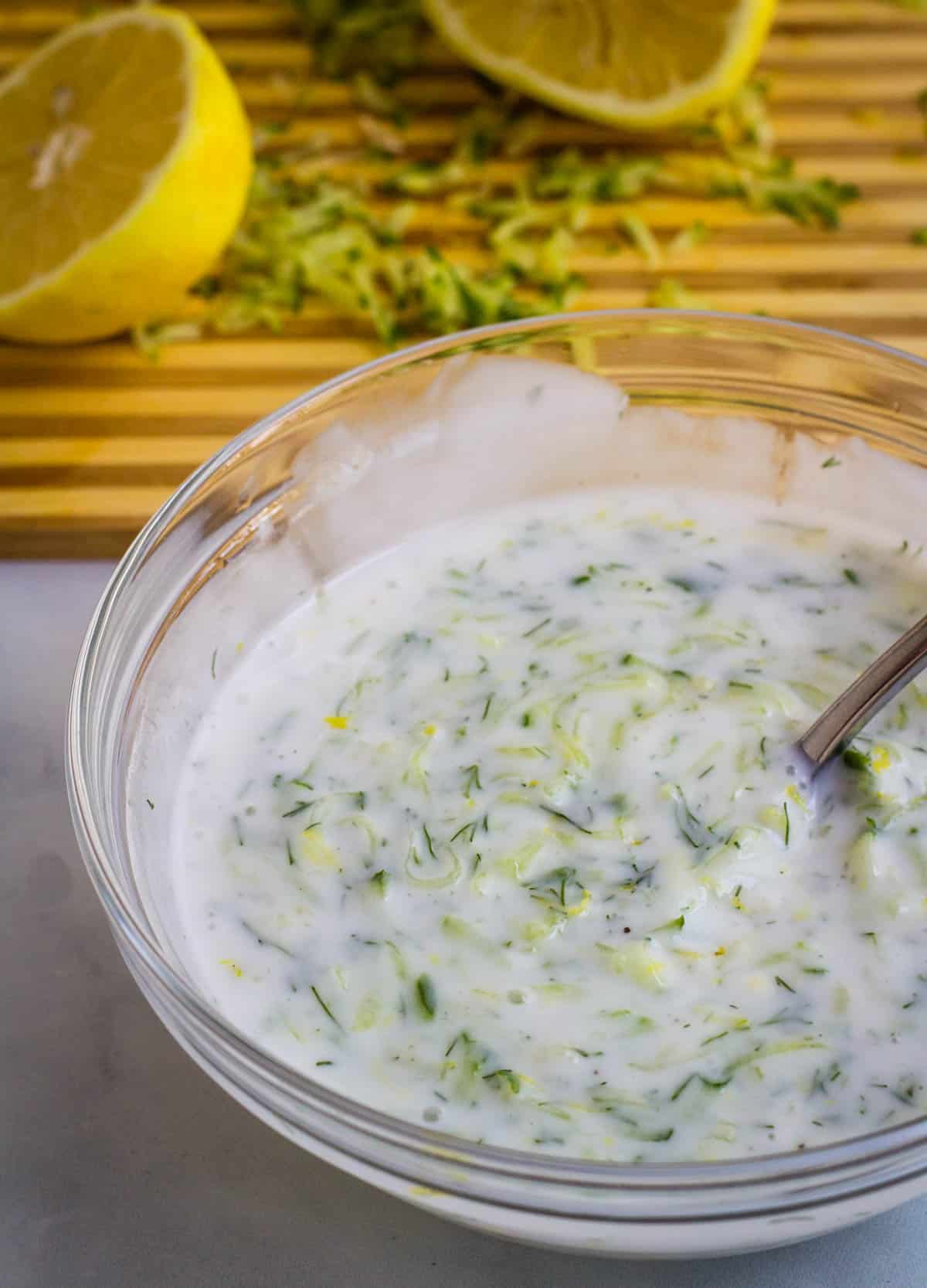 Cucumber yogurt sauce in glass bowl.