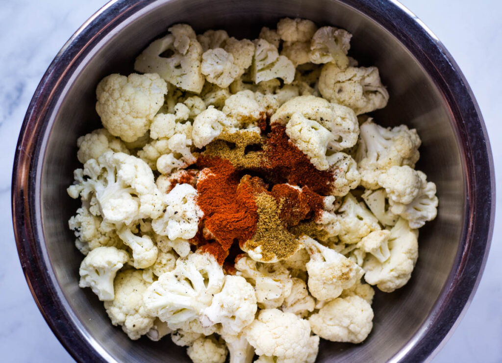 cauliflower florets in large bowl topped with spices
