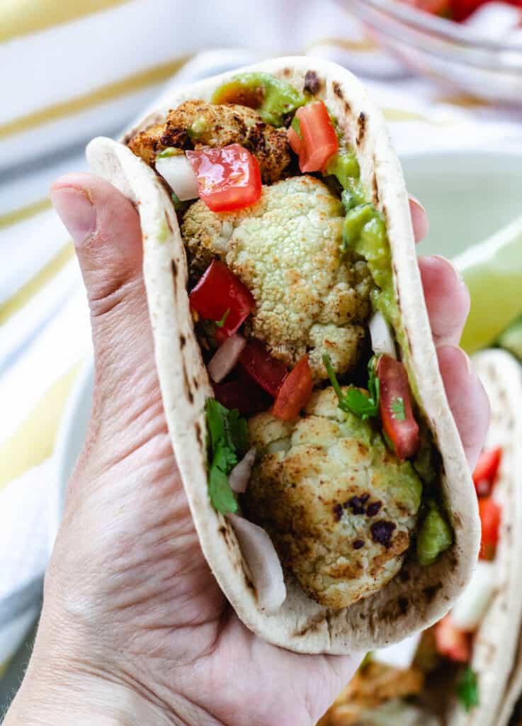 hand holding taco with cauliflower topped with tomatoes