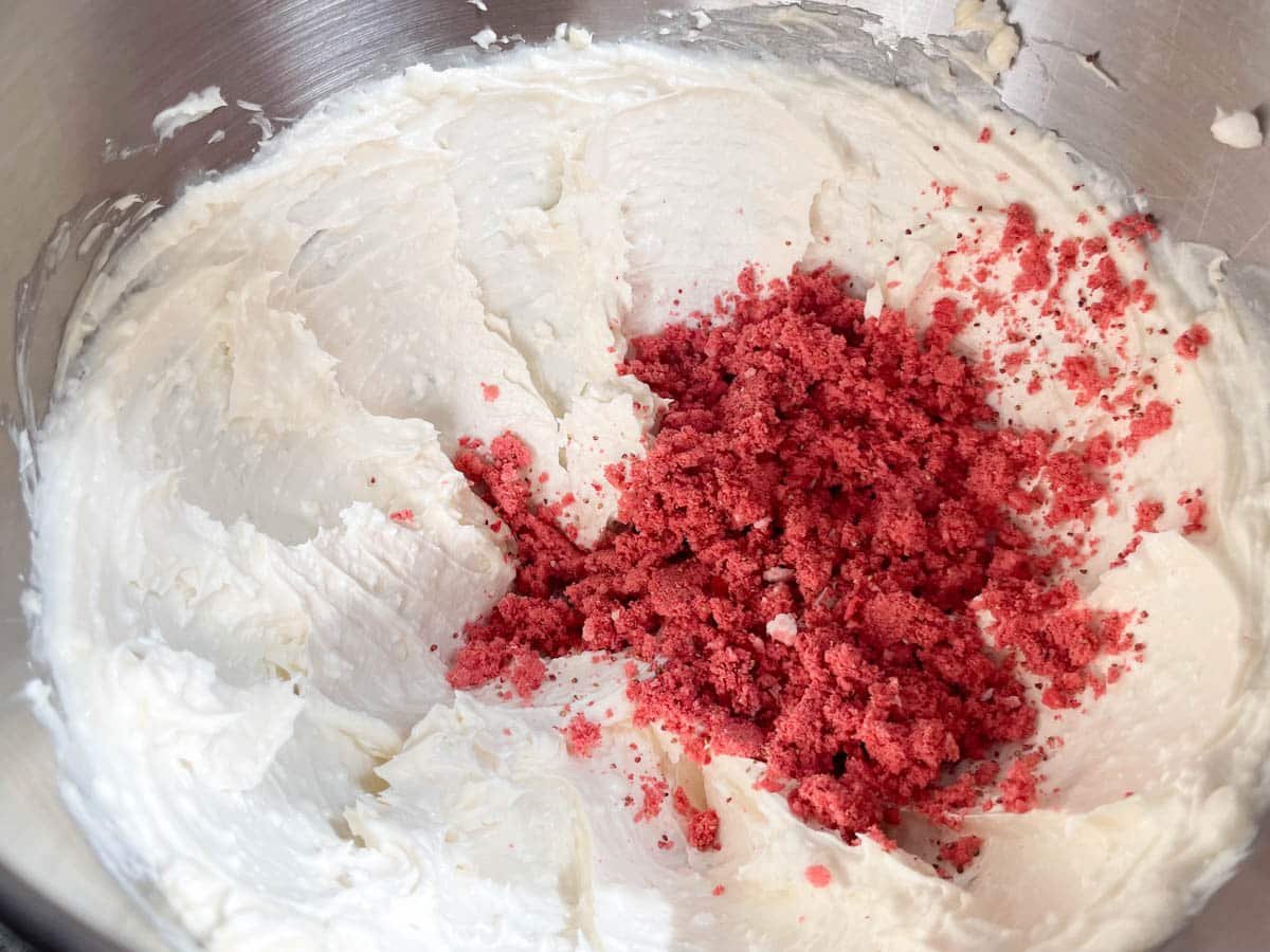 Strawberry powder added to cream cheese frosting in mixing bowl.