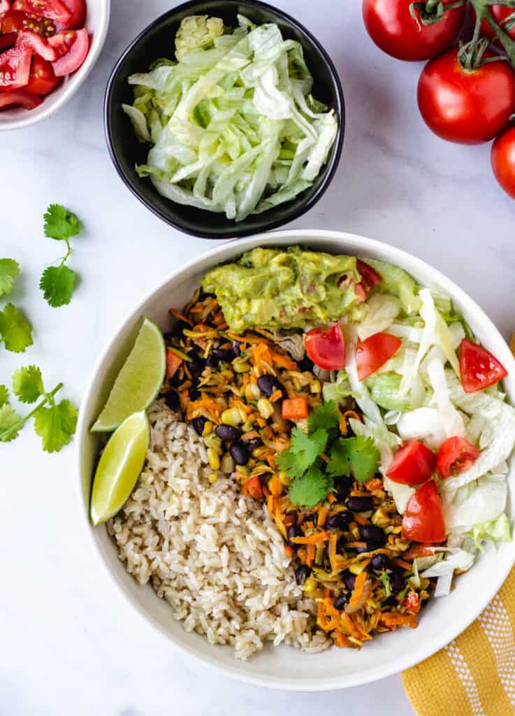 bowl of rice, mixed vegetables, lettuce, diced tomato, and wedges of lime
