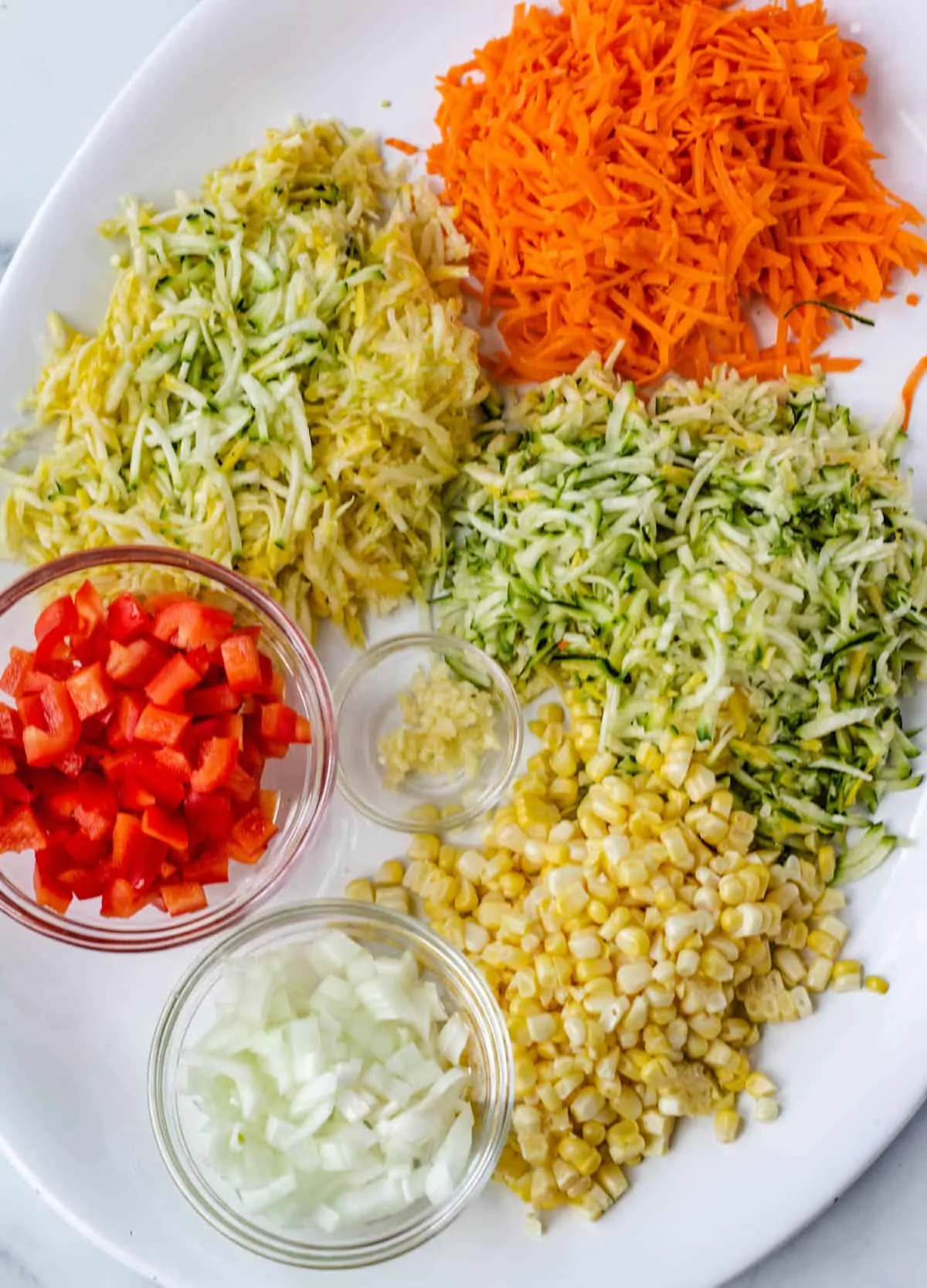shredded carrot, zucchini, and squash, diced red pepper, and onion on white platter