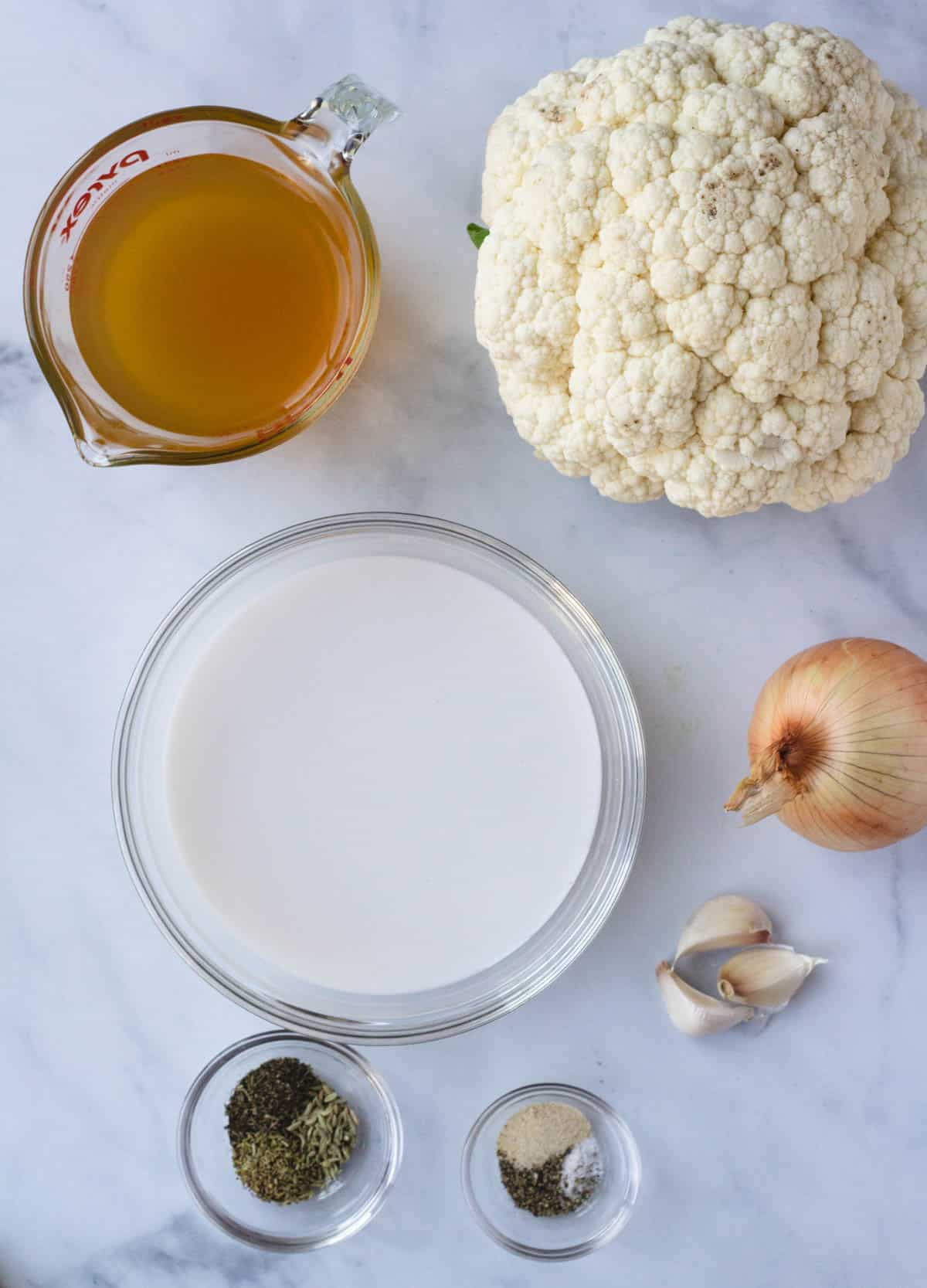 Cauliflower soup ingredients: head of cauliflower, vegetable stock, onion, garlic, coconut milk, herbs and spices.

