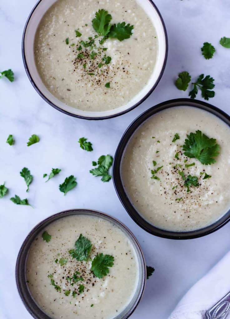 vegan cauliflower soup in three bowls topped with herbs