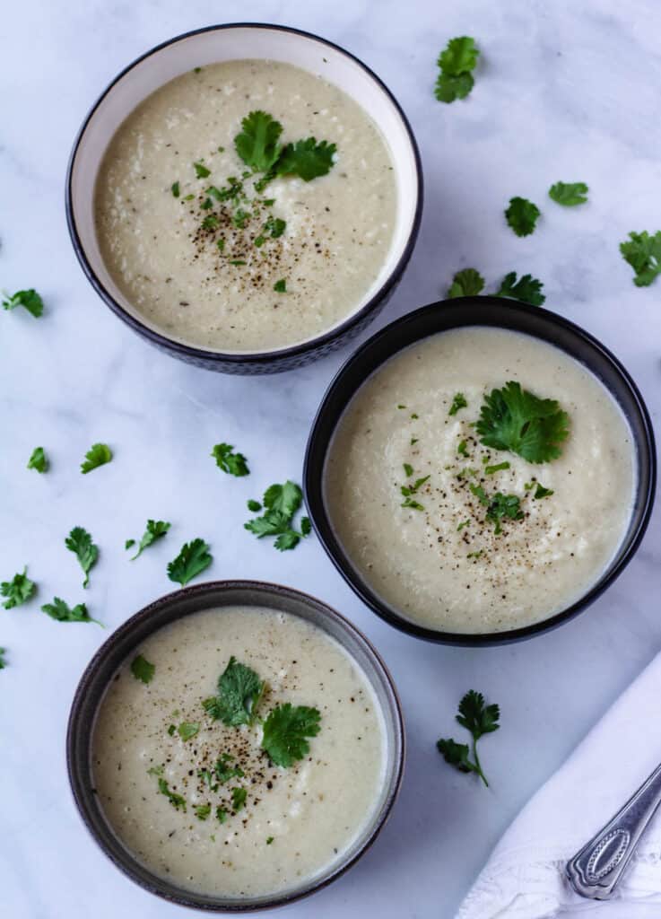 cauliflower soup in 3 bowls topped with herbs