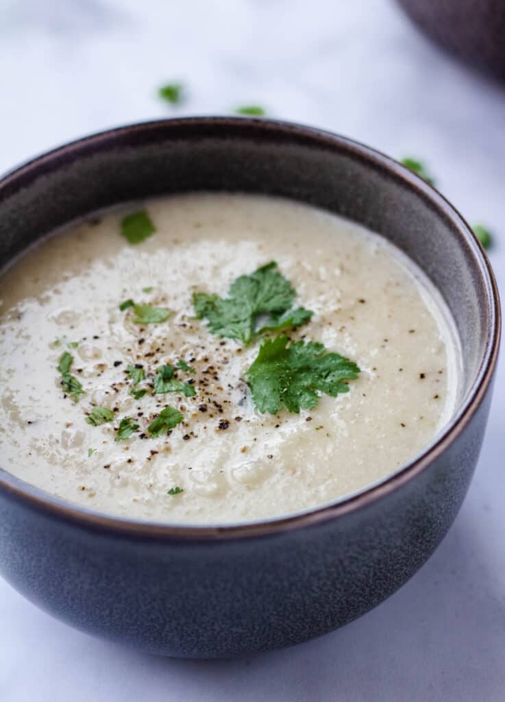 cauliflower soup in gray bowl topped with herbs
