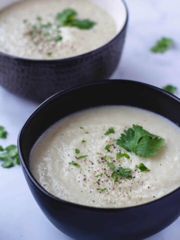 vegan cauliflower soup in black and gray bowl topped with fresh herbs