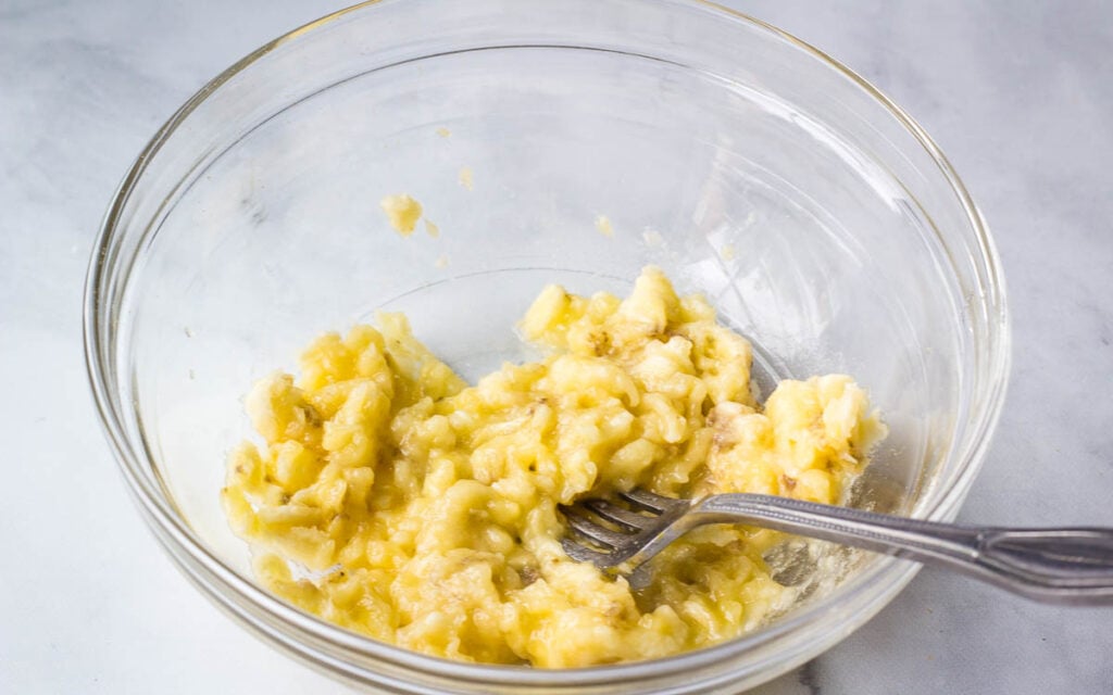 Mashed banana and fork in glass bowl.