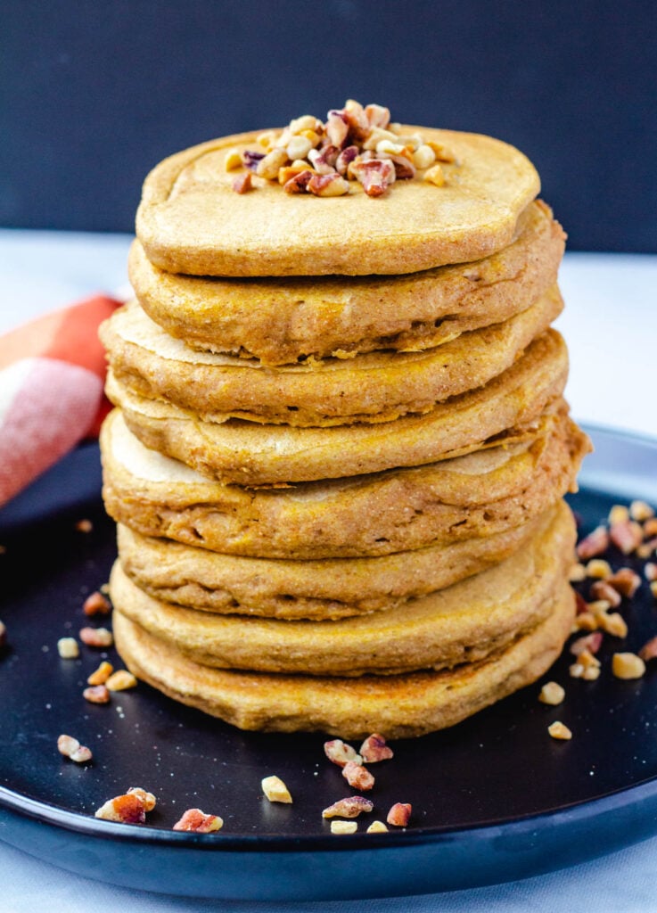 Stack of vegan pumpkin pancakes topped with nuts.