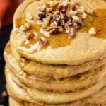 Vegan pumpkin pancakes topped with nuts and maple syrup.