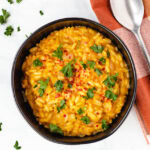 vegan pumpkin risotto in black bowl topped with parsley and red pepper flakes
