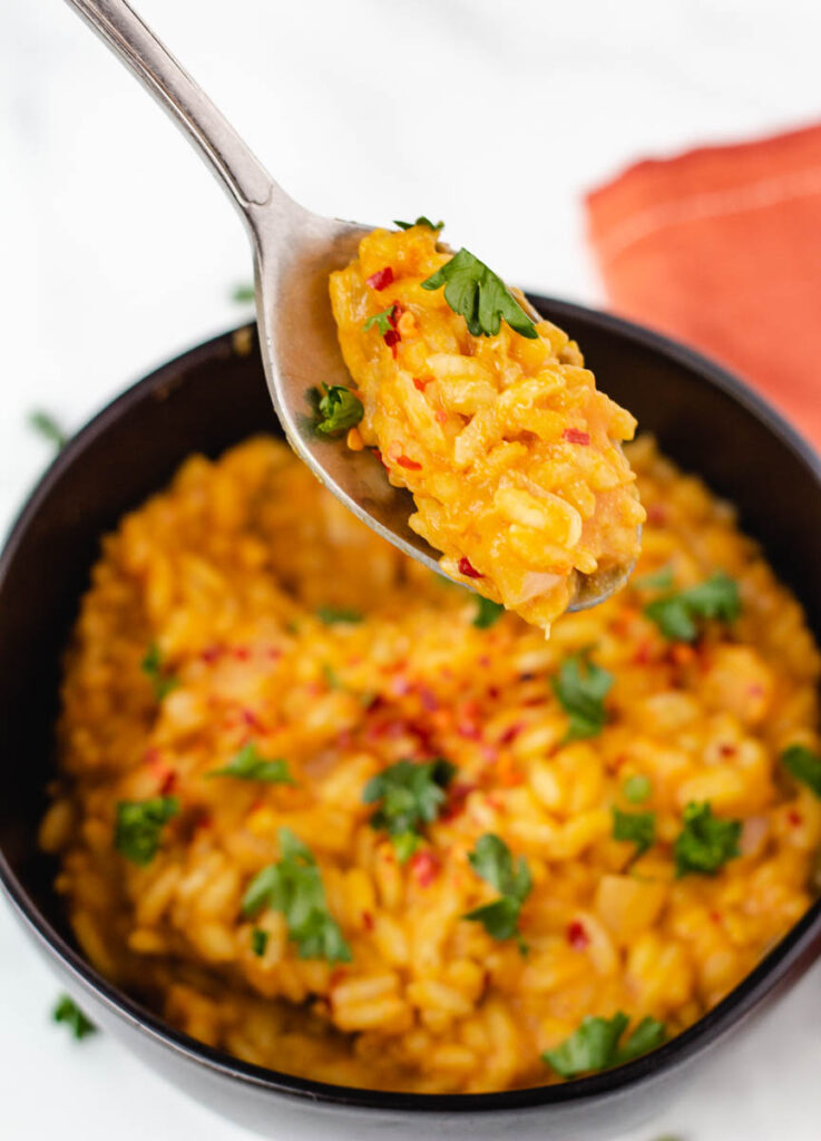 Pumpkin risotto bite on spoon held over bowl. 