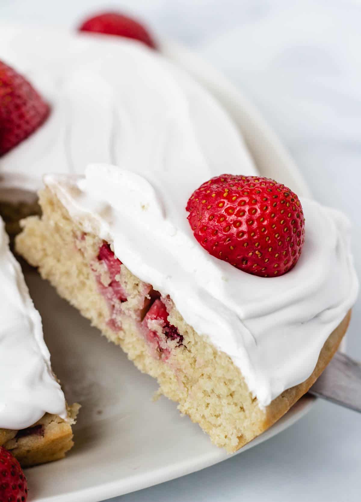 Slice of strawberry cake topped with a fresh strawberry.