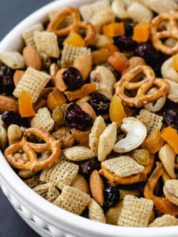 Bowl of vegan trail mix with pretzels, Chex cereal, dried fruit, and nuts.