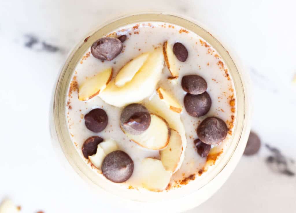 overhead of mason jar filled with banana overnight oats topped with almonds, chocolate chips, and banana slices