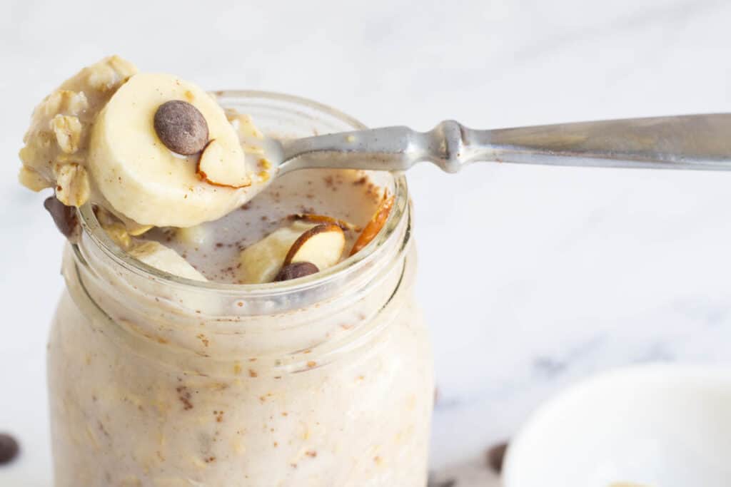 silver spoon with oatmeal on top of mason jar filled with overnight oats