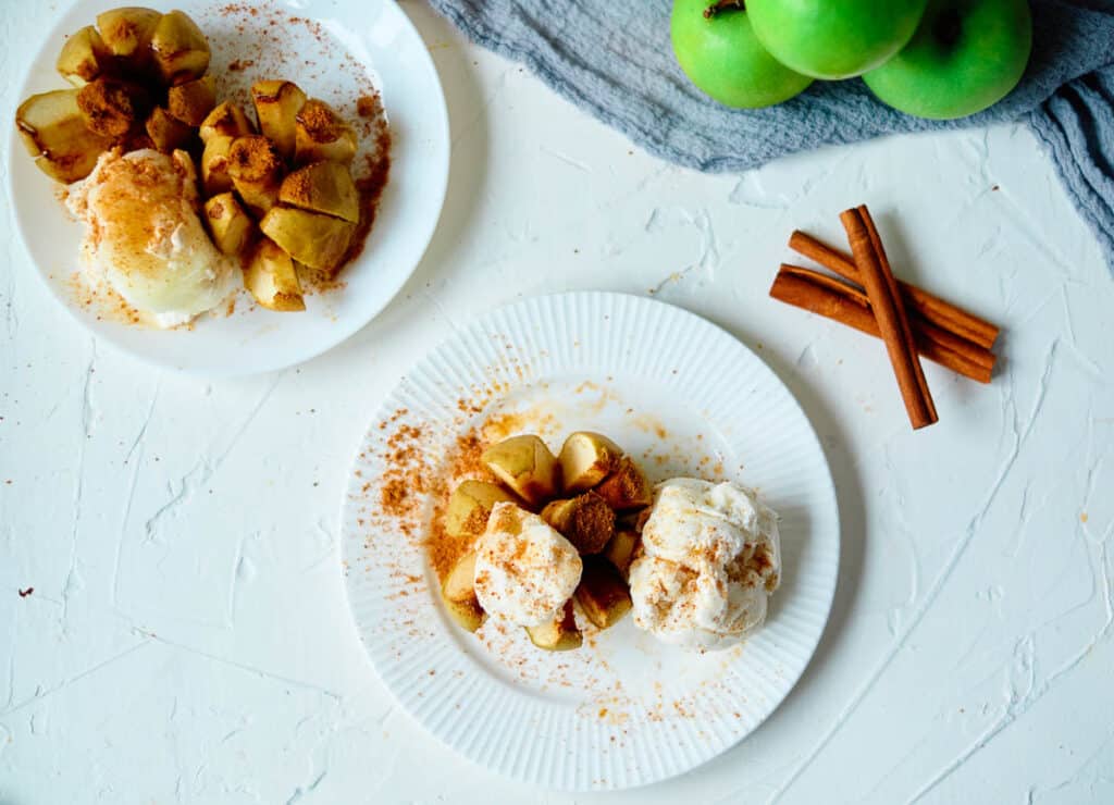 overhead of vegan baked apples with cinnamon and coconut milk ice cream with cinnamon sticks and apples