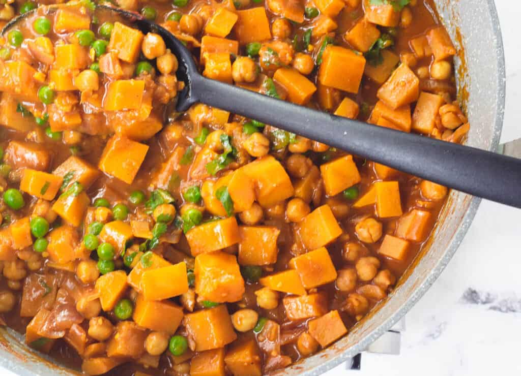 butternut squash and chickpea curry with peas and cilantro in pot with spoon