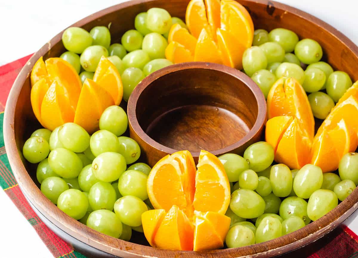 Sliced oranges surrounded be green grapes in round serving platter.
