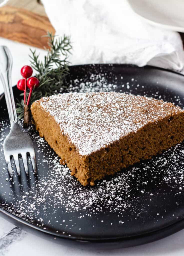 vegan ginger cake on black plate topped with powdered sugar