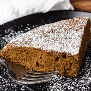 vegan ginger cake slice dusted with powdered sugar on black plate