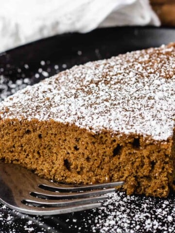 vegan ginger cake slice dusted with powdered sugar on black plate
