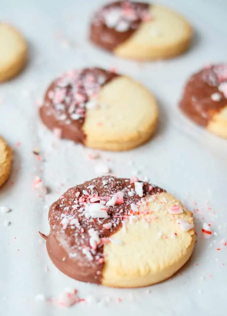 cookies dipped in chocolate topped with crushed peppermint on parchment paper