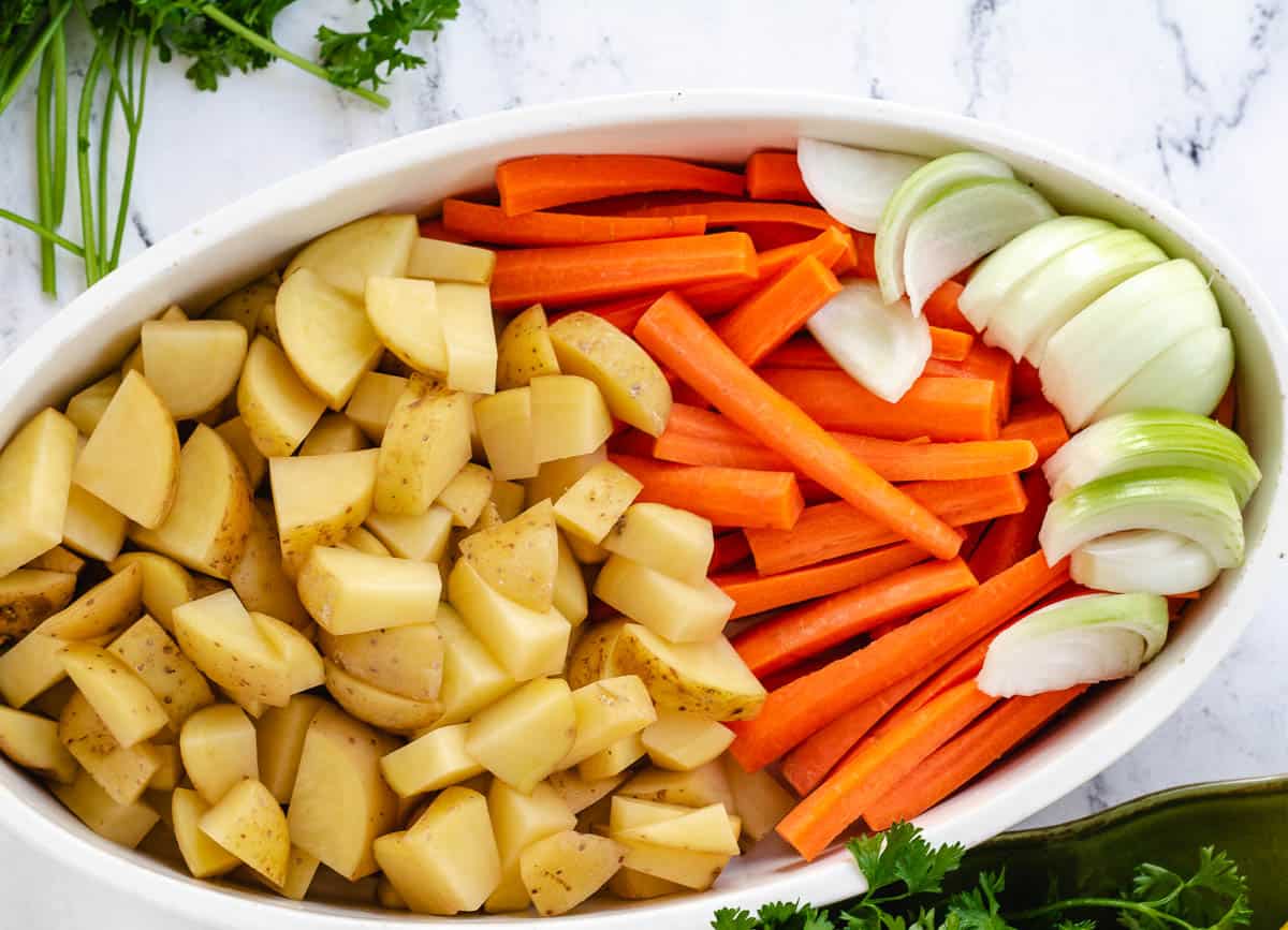 Chopped potatoes, carrots and onions in a baking dish. 
