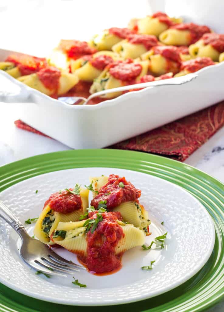 three stuffed jumbo shells on white plate with baking dish in the background
