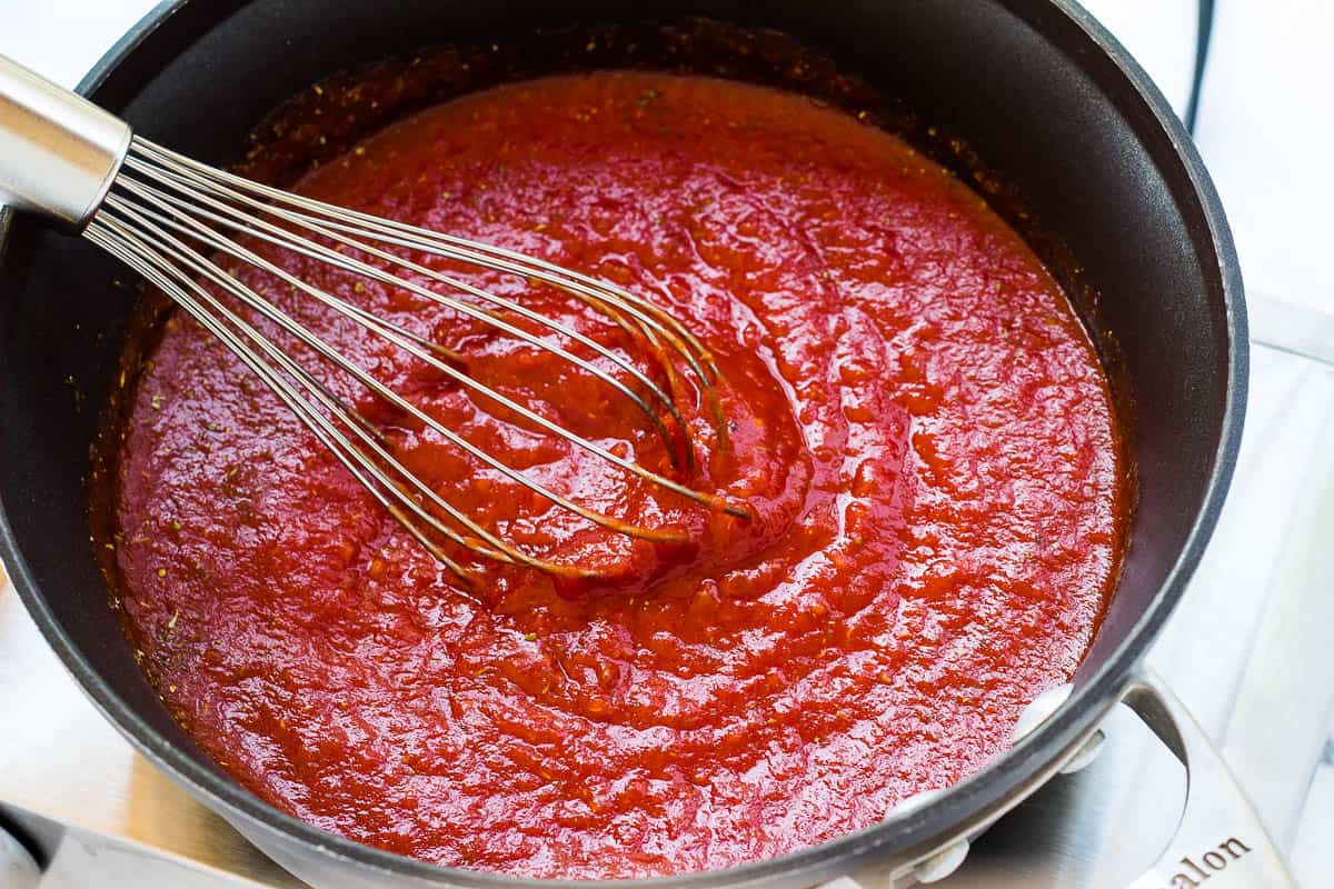 Tomato sauce in pot with whisk.
