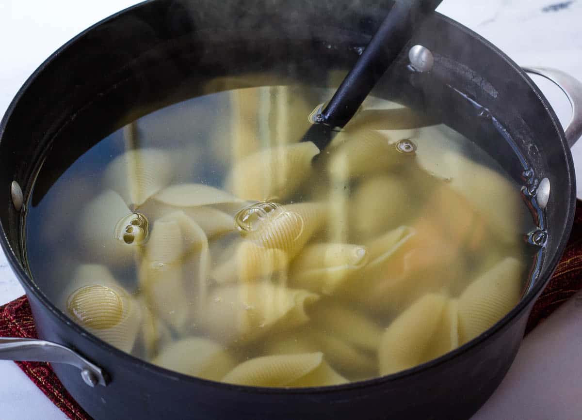 Jumbo shells boiling in large pot of water.
