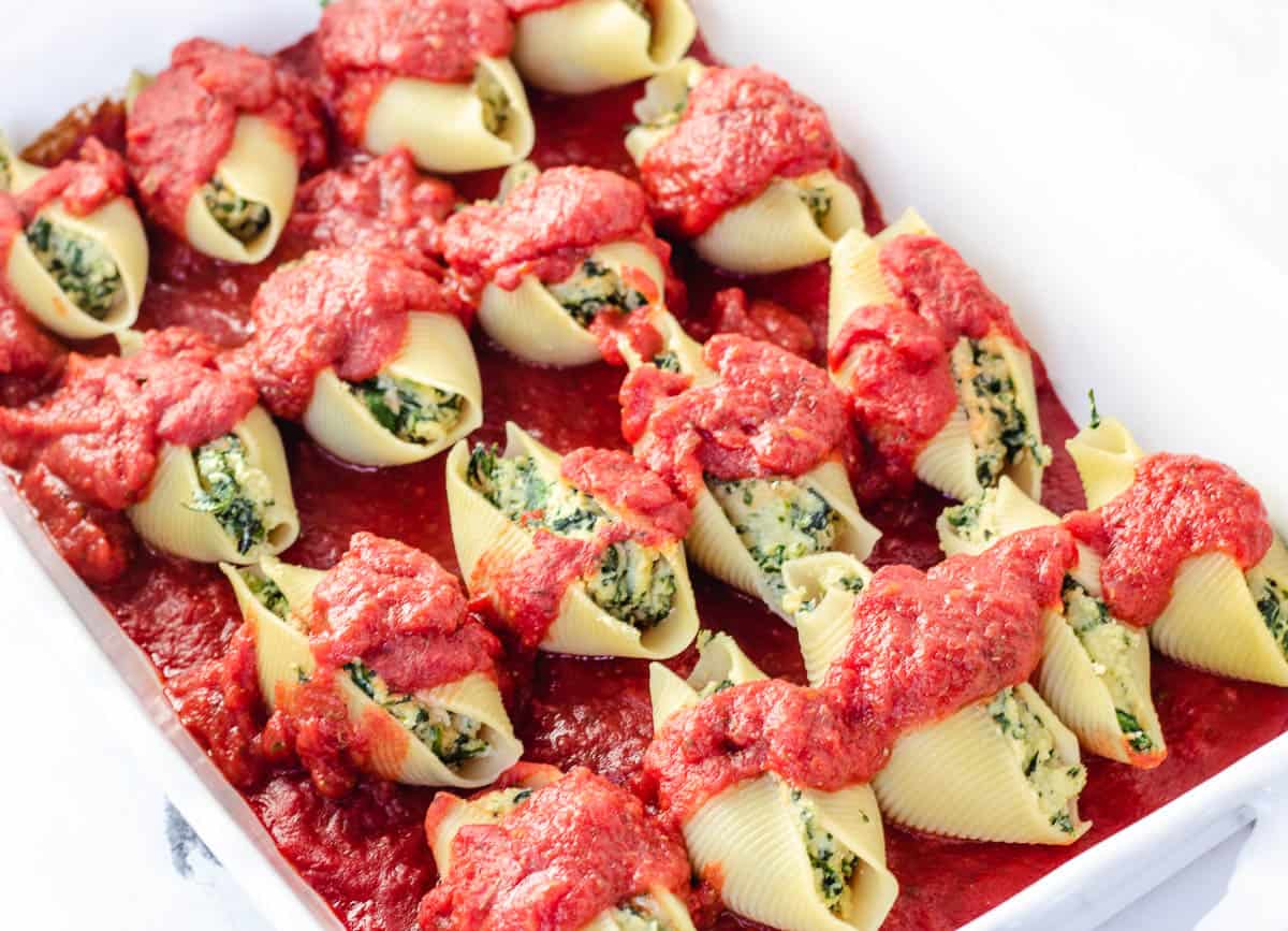 Vegan stuffed shells in baking dish topped with tomato sauce.
