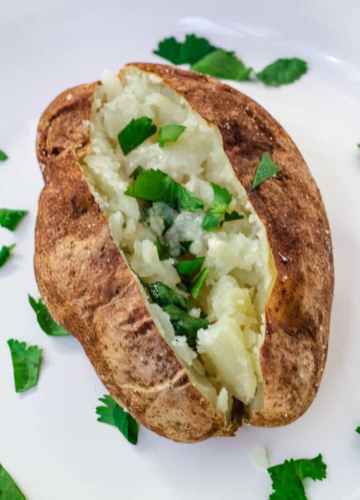 air fryer baked potato on white plate topped with butter and fresh herbs