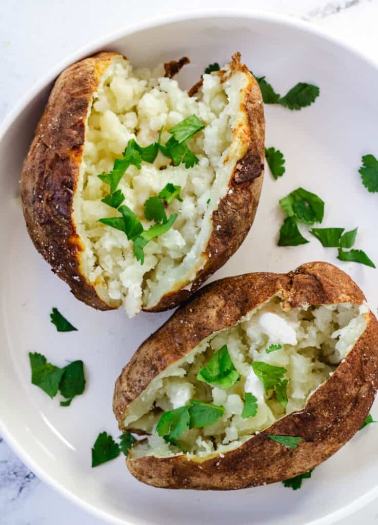 two baked potatoes on a white plate topped with butter and fresh herbs