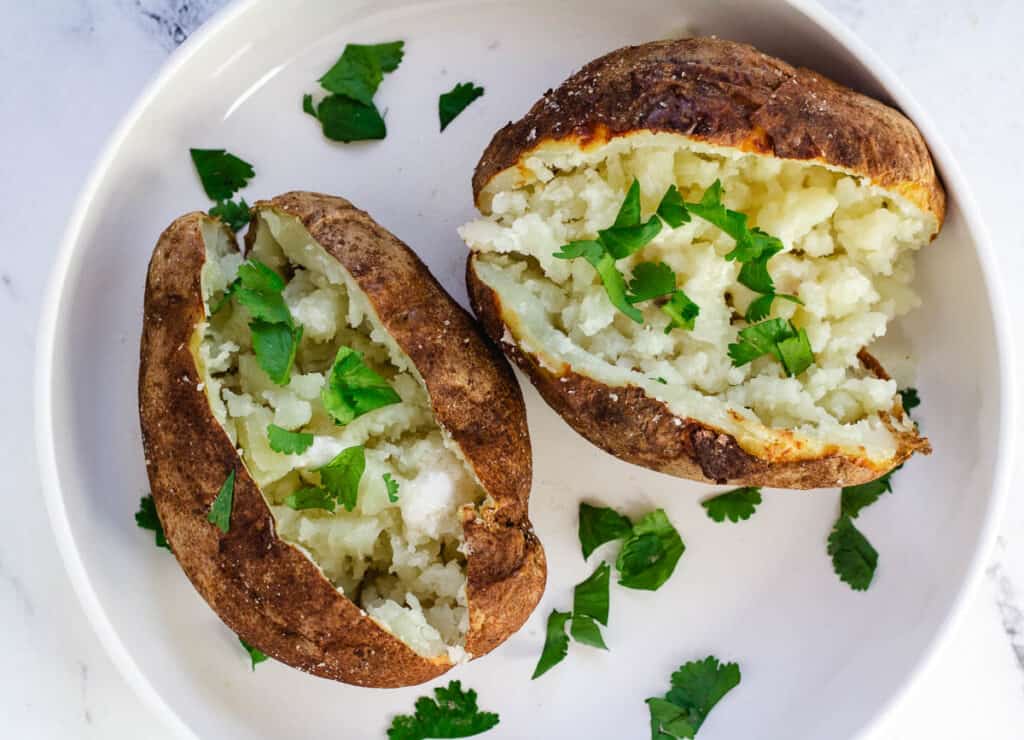 baked potatoes on white plate topped with butter and herbs
