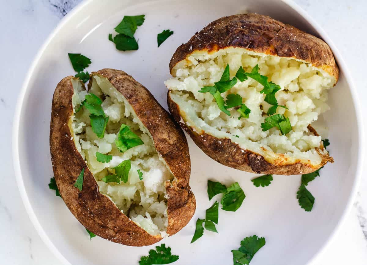 Two baked potatoes on a white plate.