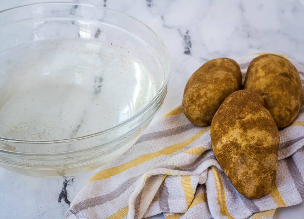 russet potatoes on dish towel next to bowl of water