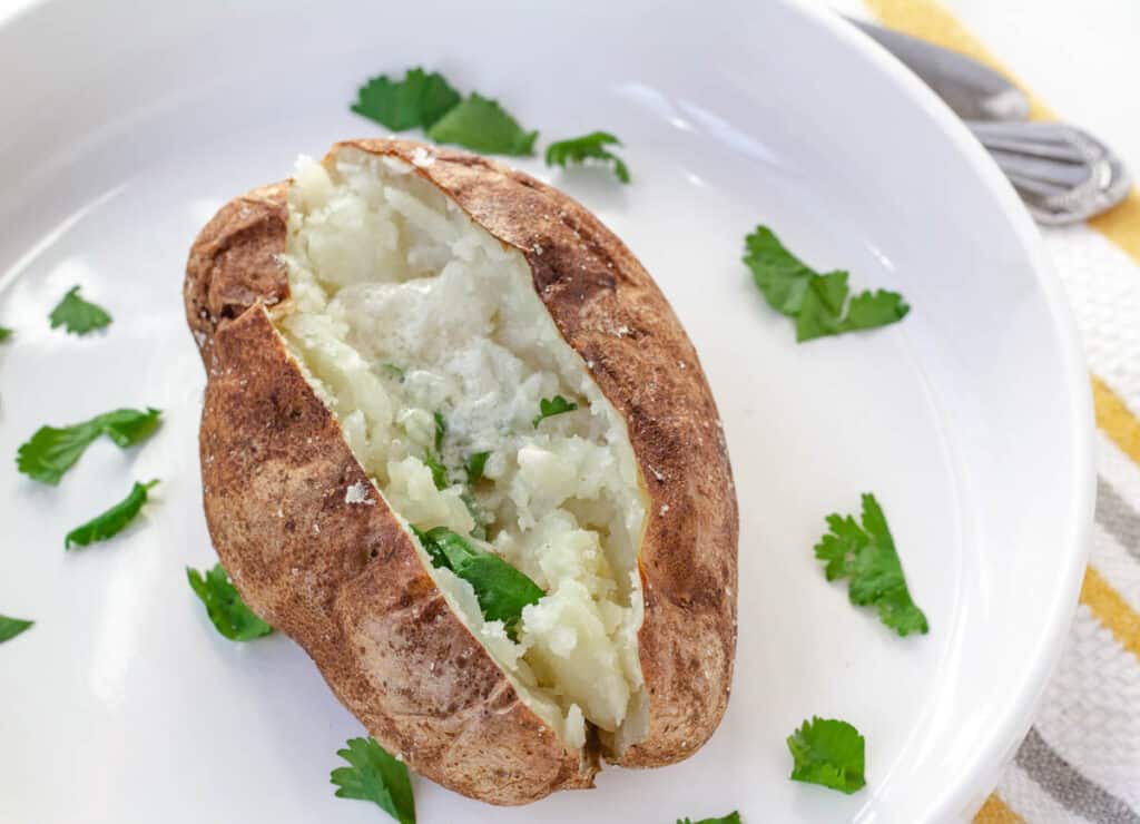 baked potato on white plate topped with herbs