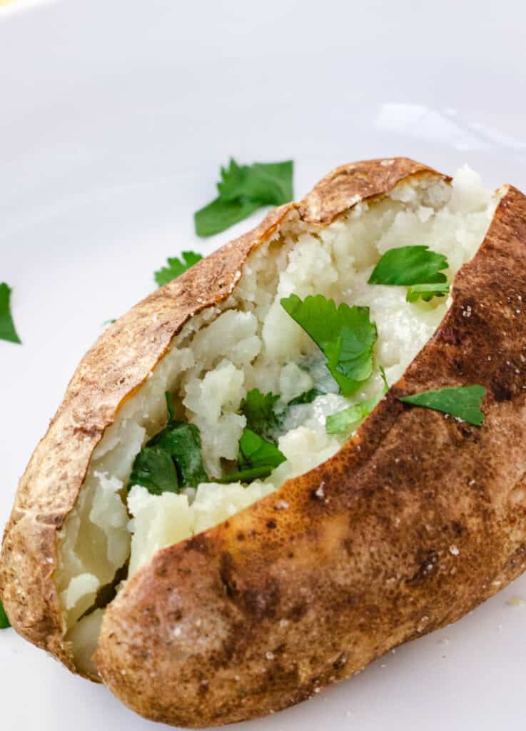 air fryer baked potato topped with butter and fresh herbs