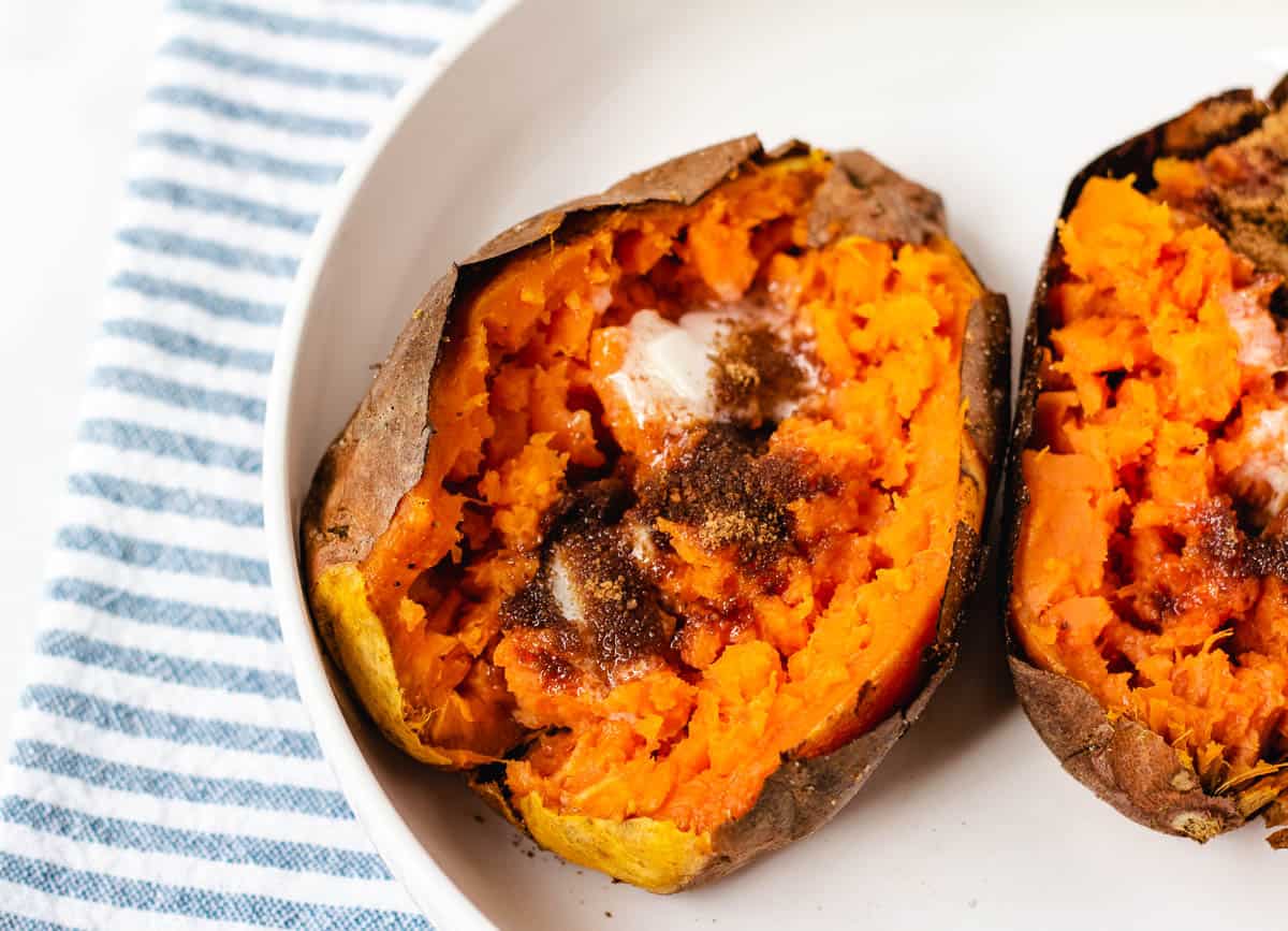 Air fryer baked sweet potato in white bowl topped with butter and brown sugar.