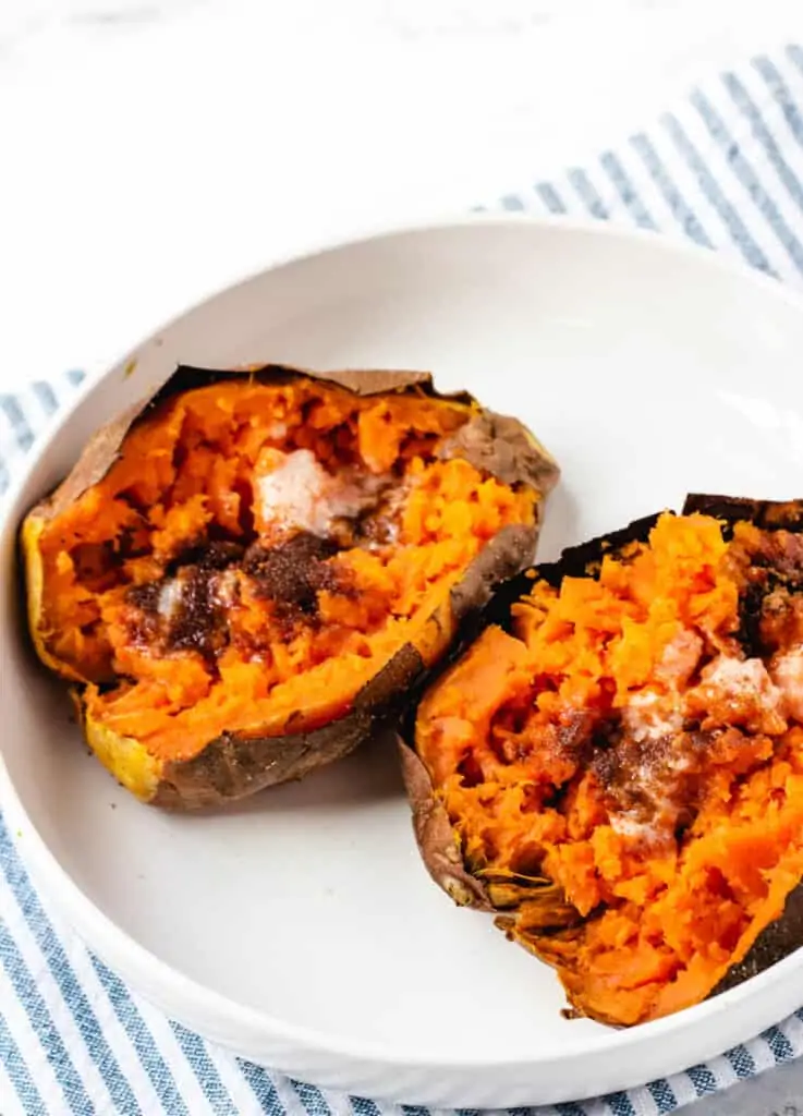 2 air fryer baked sweet potatoes in white bowl topped with butter and brown sugar