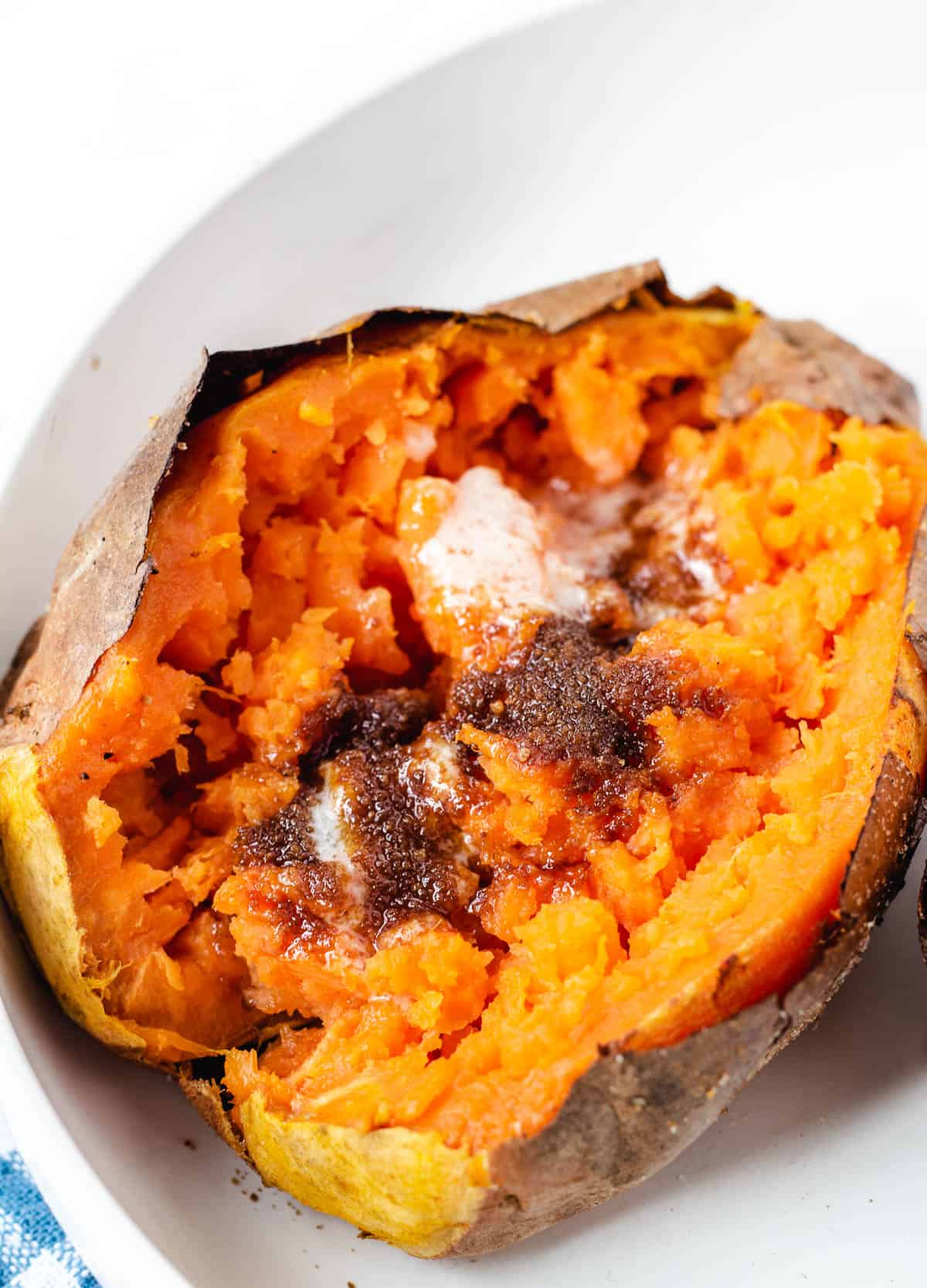 Air fryer baked sweet potato with butter and brown sugar in a white bowl.