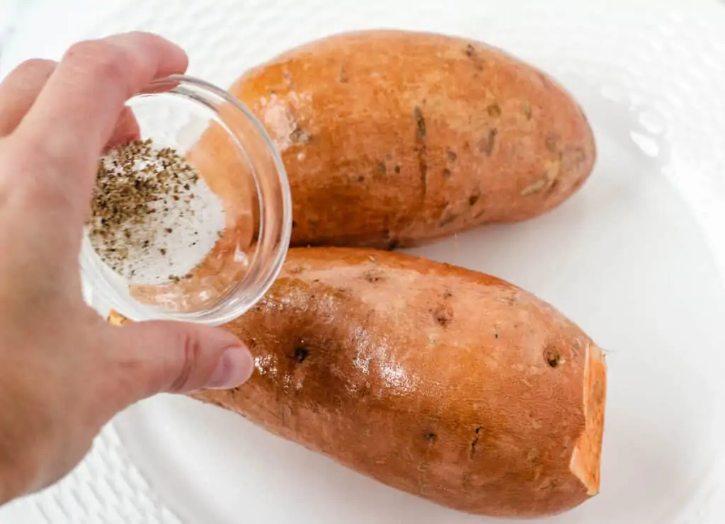 hand sprinkling salt and pepper on sweet potatoes