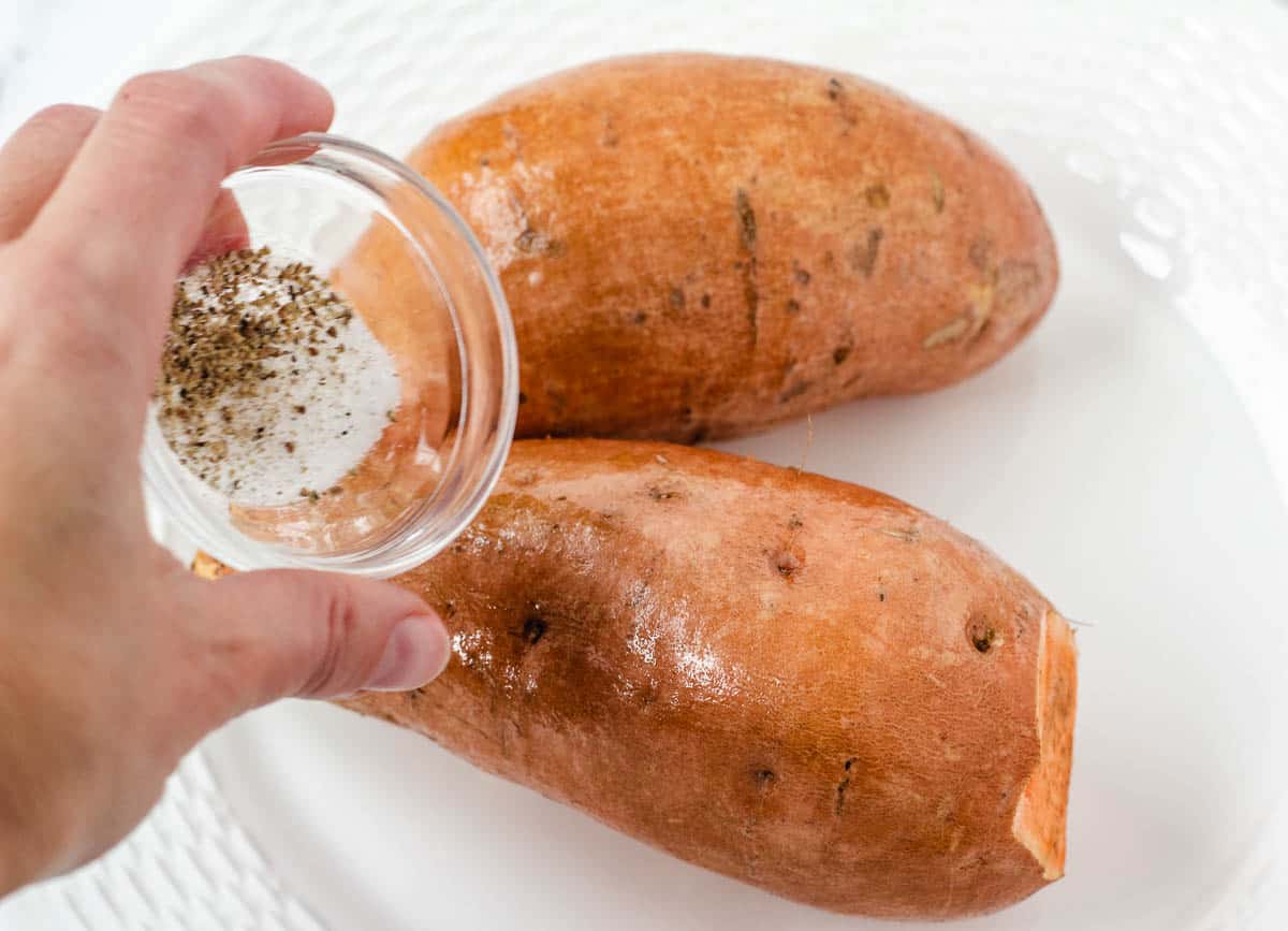 Hand sprinkling salt and pepper on sweet potato.