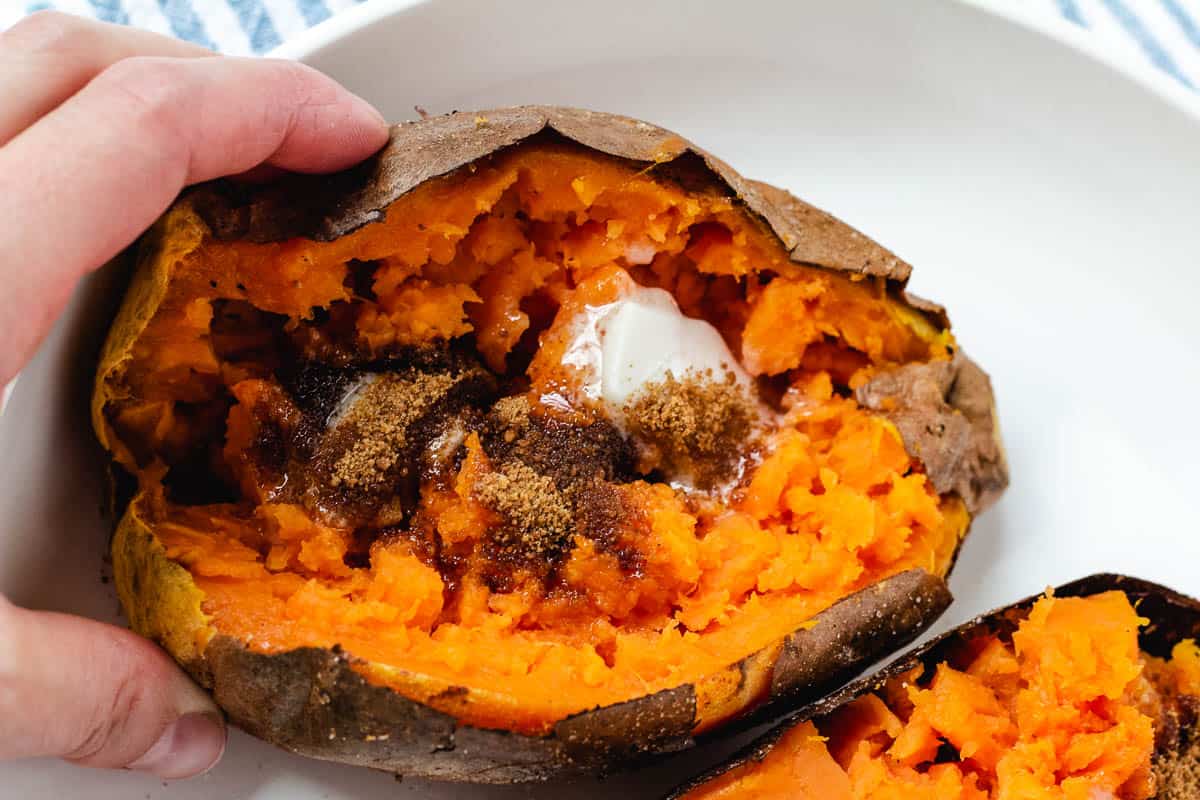 Hand holding baked sweet potato topped with butter and brown sugar.