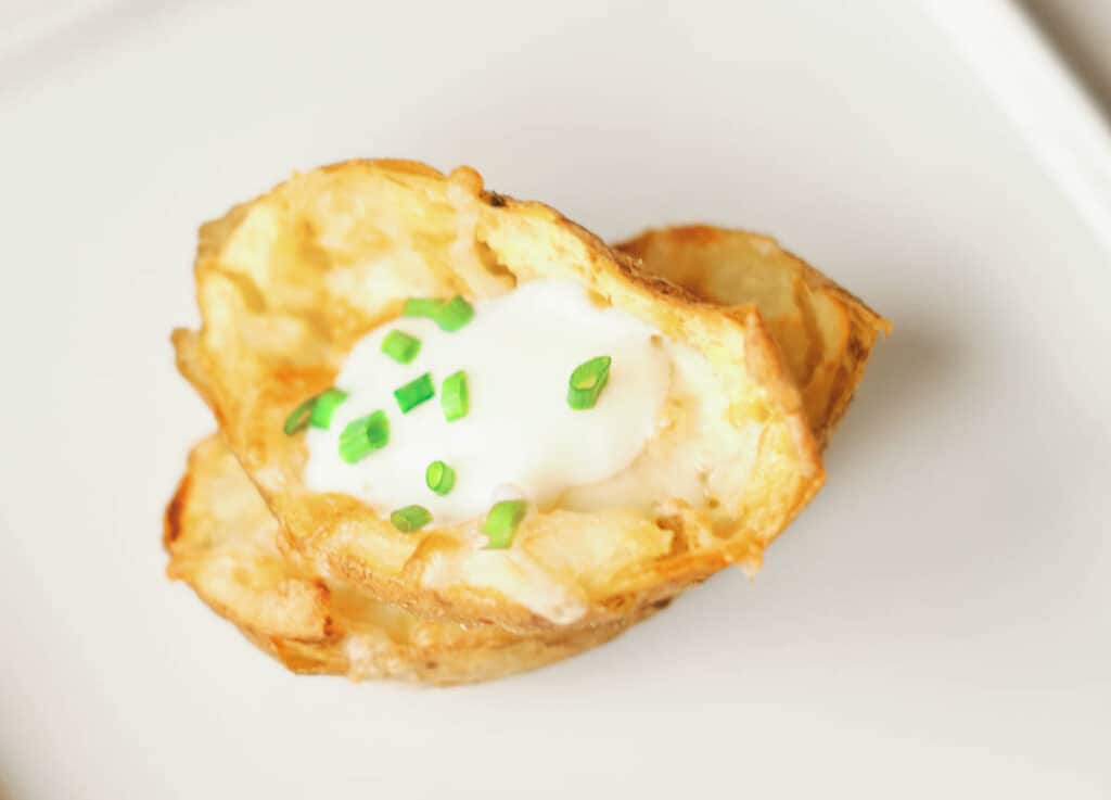 close up of two potato skins stalked on top of one another topped with sour cream and chives